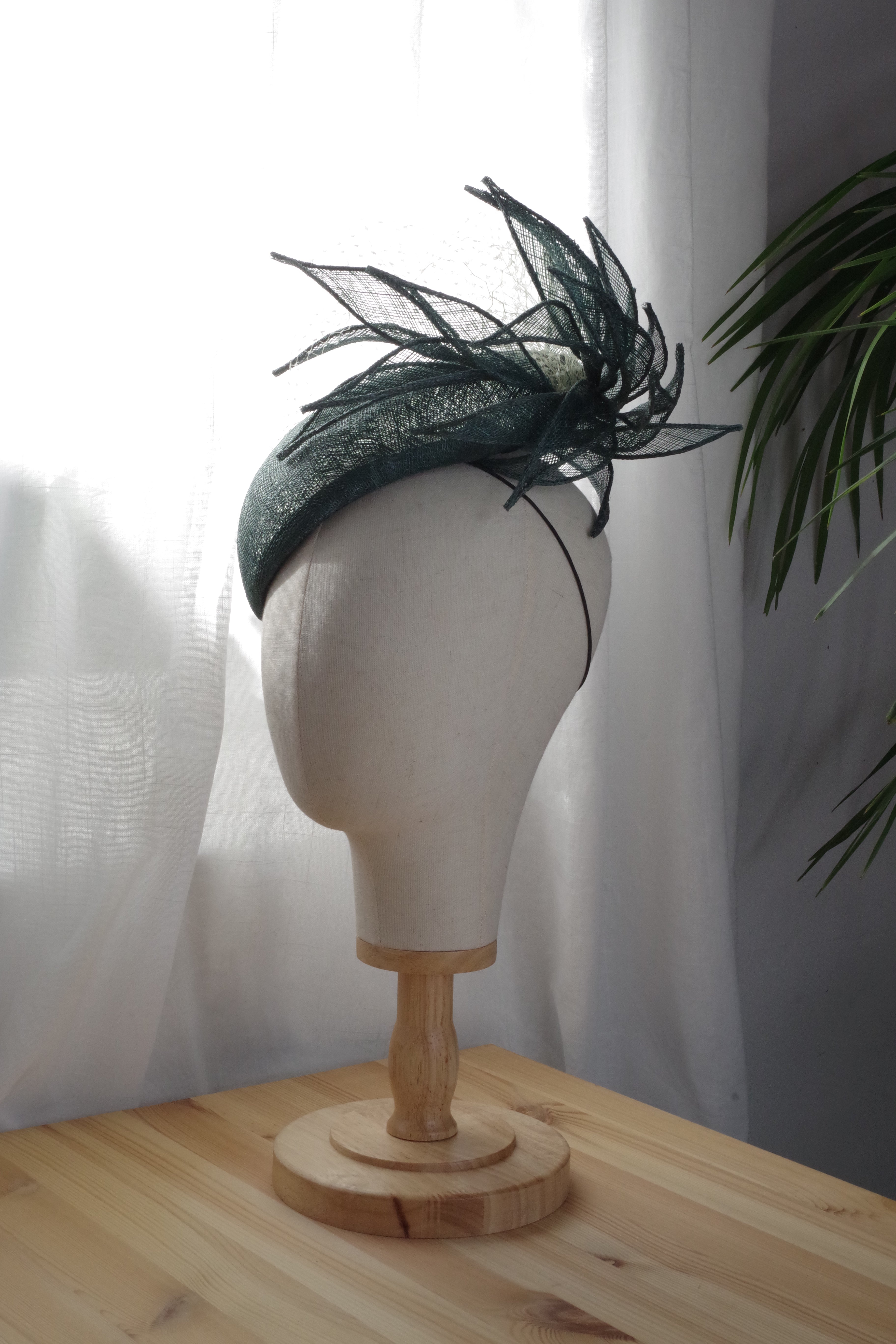 Side view of the Whispering Fern handcrafted green sinamay cocktail hat by MICHAETT, showcasing sculptural leaf-inspired detailing, delicate veiling and the elegant curved silhouette.