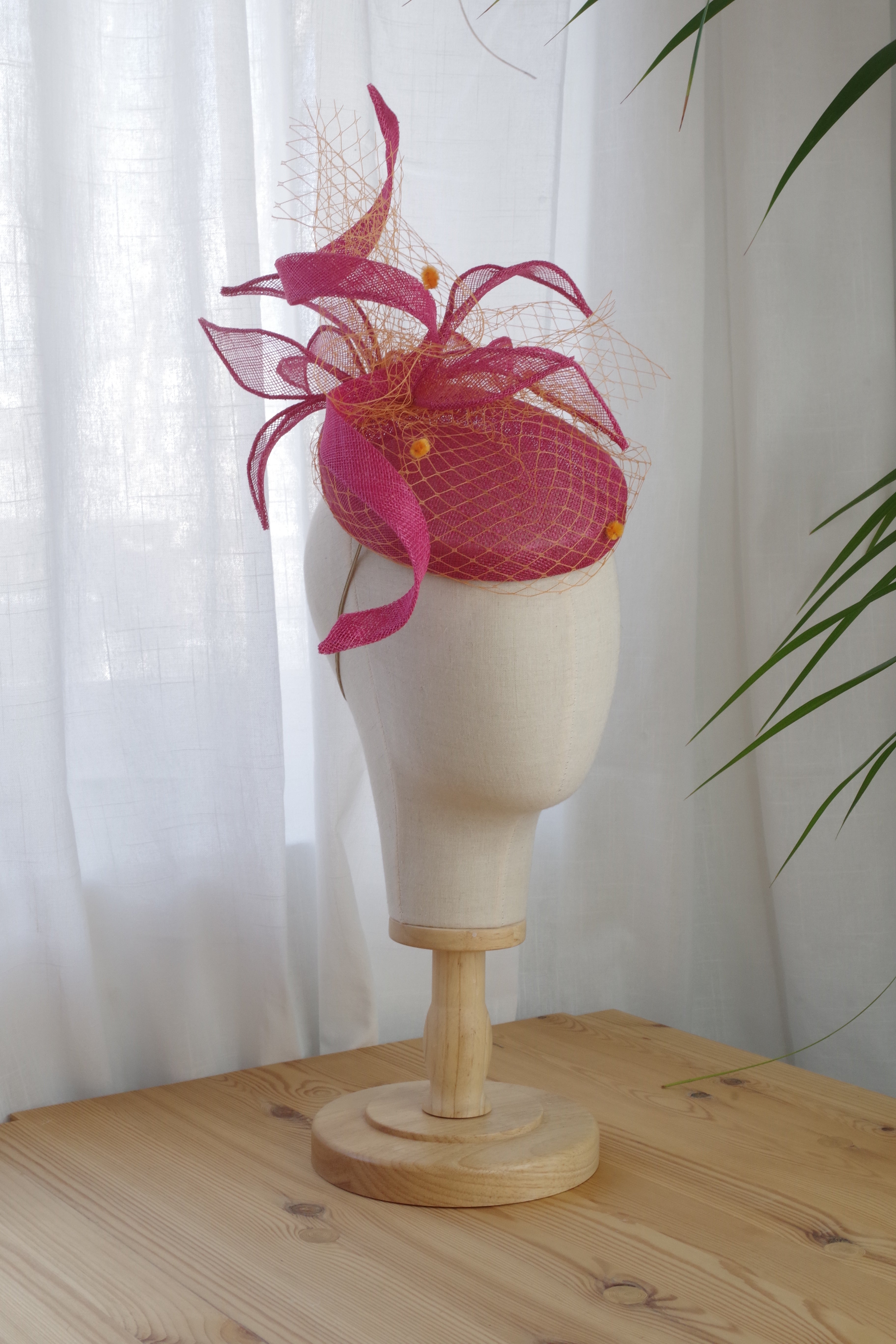 Side view of pink sinamay cocktail hat with orange veiling and sculptural loops by MICHAETT