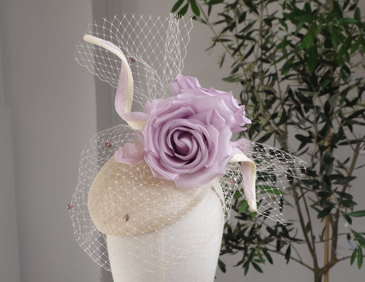 Sample hat for the MICHAETT millinery workshop in Bowral – a petite natural sinamay cocktail hat with a curled lavender-edged sinamay band, beaded veiling and lilac roses, shown on a millinery head.